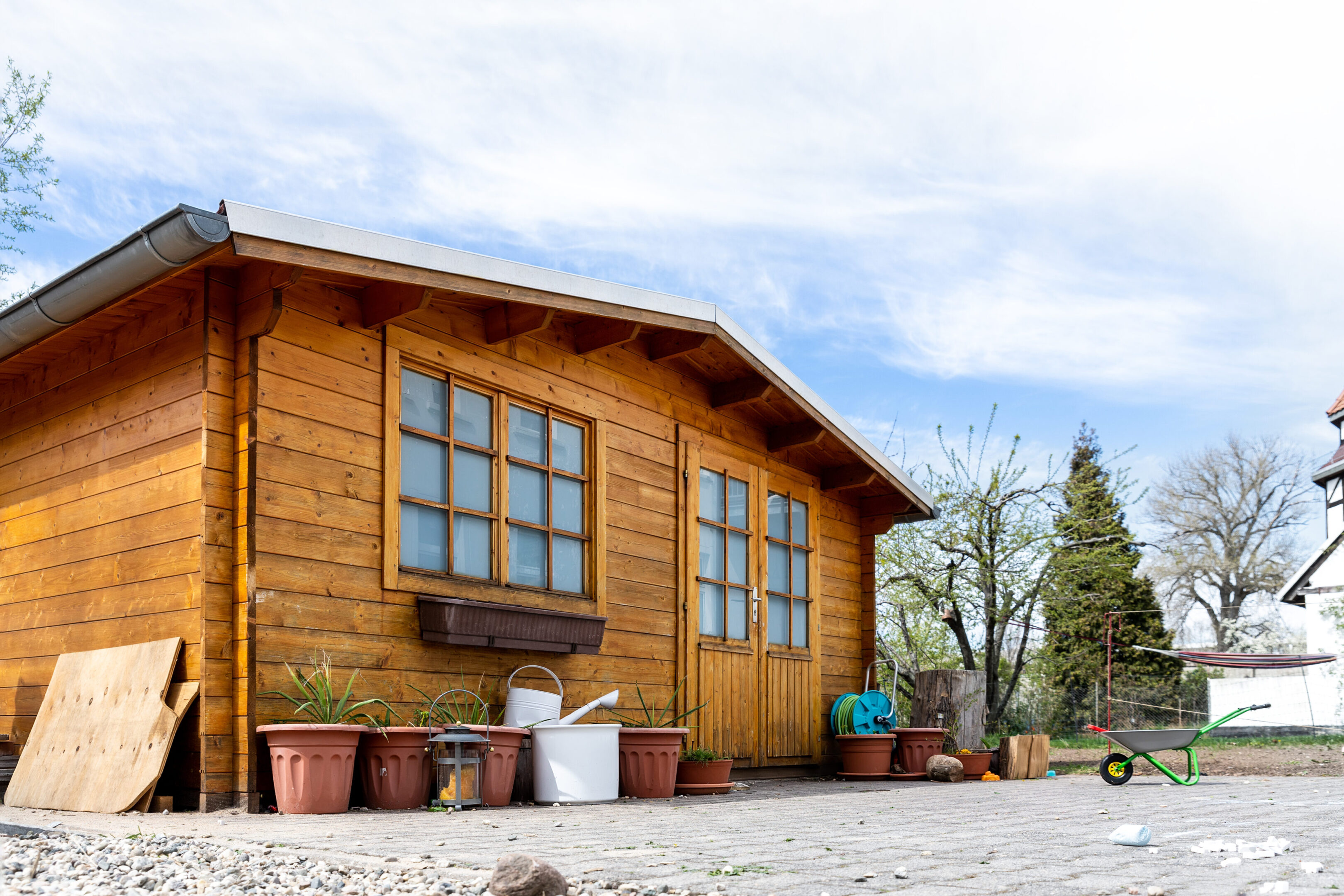 Small beautiful wooden house shed or storage hut for garden tools equipment and bicycles at backyard at beautiful american or european countryside backyard. Cozy rural yard stuff warehouse A wooden house with many windows and potted plants.